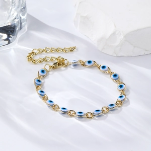 Detail of gold evil eye bracelet with blue beads on white marble with water light effects
