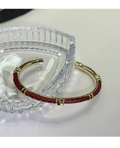 Dettaglio del bracciale in pelle intrecciata rossa con decori metallici dorati a forma di X