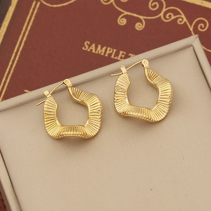 Close-up of irregular geometric gold earrings with textured wavy surface and metal finish