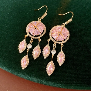 Detail of vintage gold earrings with pink gemstones and tassels on green velvet