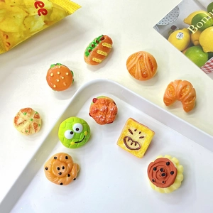 Macro shot of cute miniature hamburger and pastry pins with cartoon faces on a tray
