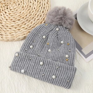 Detail of grey knitted hat featuring fluffy fur pompom and delicate pearl bead accents