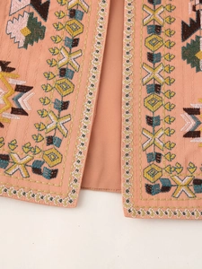 Detail shot of ethnic geometric embroidery on pink vest fabric with vibrant threads
