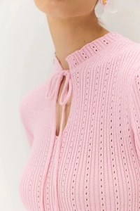 Dettaglio dell'abito in maglia traforata rosa con scollo a balze e laccio frontale