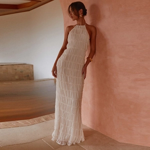 Detail of white halter neck maxi dress with pleated texture against a warm wall