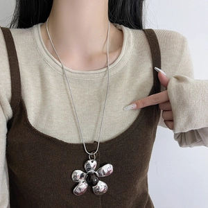 Detail of vintage silver flower pendant necklace worn over a stylish brown knit vest