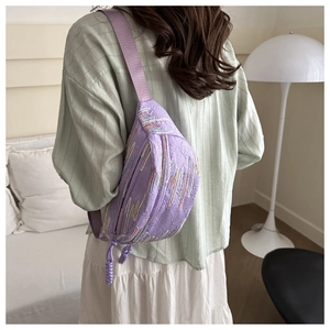 Detail of purple pleated canvas chest bag featuring rainbow embroidery and woven strap