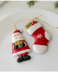 Detail of glossy ceramic Santa and gift stocking pendants with gold cords on a white plate