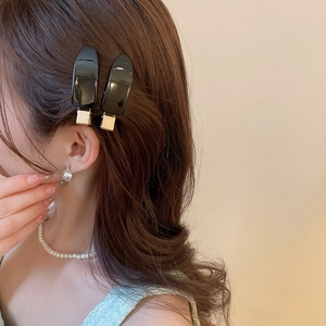 Close-up of glossy black teardrop hair clips with metal base worn on brunette hair