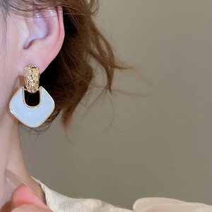 Close-up of gold geometric drop earrings with cream inlay worn by a model