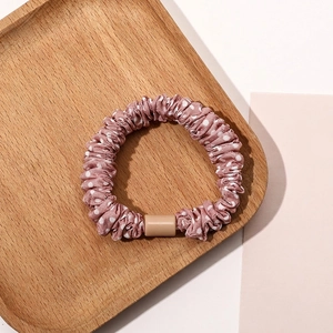 Close-up of pink polka dot satin scrunchie with smooth resin buckle on wood tray