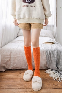Close-up of bright orange coral fleece knee-high socks worn with cozy plush slippers