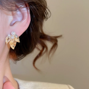 Gros plan sur une boucle d'oreille feuille dorée avec perles et détails en diamant