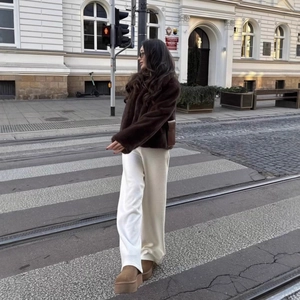 Women's dark brown faux fur short coat styled with white wide-leg pants and platform boots