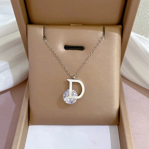 Detailed macro view of silver D-letter pendant necklace with round zircon in a beige jewelry box