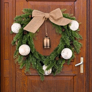 Christmas wreath with pine cones and white balls hanging on a dark brown wooden door