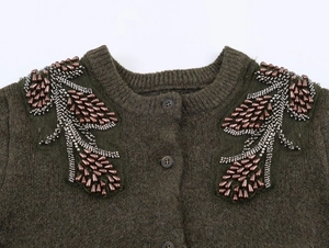 Dettaglio del cardigan in maglia verde oliva con perline di rame e tubicini argentati