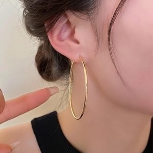 Close-up of a model wearing a large polished golden hoop earring in a minimalist style
