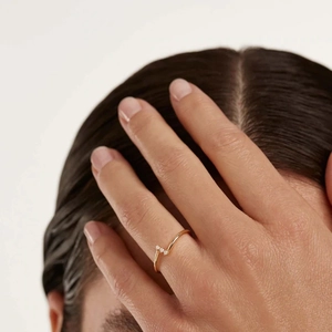 Close-up of a delicate V-shaped gold ring with three small diamonds worn by a model