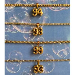 Detailed display of four gold year number pendants with various chain styles on blue background