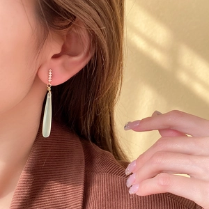 Detail of silver needle zircon drop earrings featuring a light green teardrop pendant on model