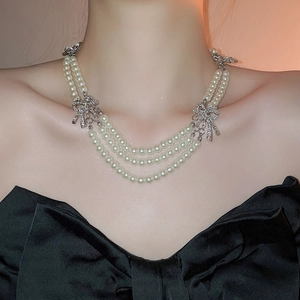 Close-up of layered pearl necklace with silver bowknot pendant on female model