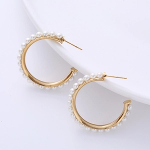 Detail of C-shaped gold hoop earrings featuring elegant white pearls on a white plate