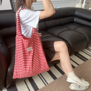 Detail of red gingham pattern tote bag with woven label on a black leather sofa