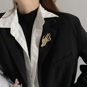 Detailed close-up of a high-polish gold palm brooch pinned on a chic black blazer