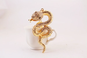 Detailed view of a gold snake pendant with sparkling rhinestones on a white cup