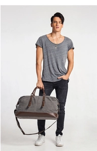 Man carrying a large grey canvas travel bag with brown leather details in studio