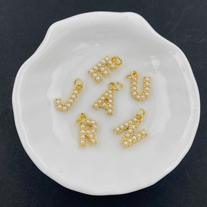 Close-up of gold-plated initial pendants with pearls in a white ceramic dish