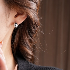 Macro shot of silver metallic bean earrings worn on a model, showcasing sleek polished finish
