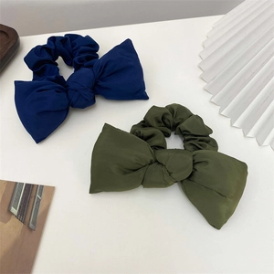 Detail of dark blue and army green bow scrunchies in smooth satin fabric on white desk