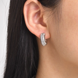 Close-up of silver hollow C-shaped hoop earring with textured threaded detail on ear
