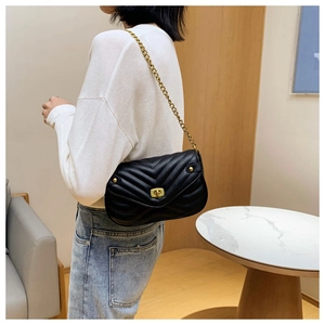 Detail of a black V-quilted leather shoulder bag with a gold chain strap on a model