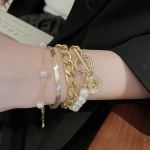 Close-up of layered gold chain bracelets with pearls and coin charm on woman's wrist