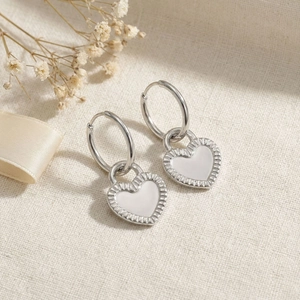 Detail of silver heart hoop earrings with white enamel on a soft beige fabric background