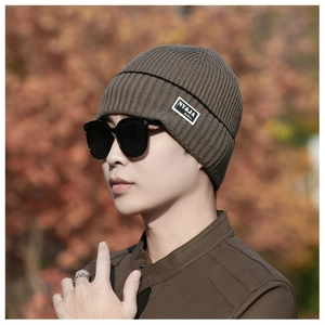 Detail of a dark brown knit beanie with a square white fashion label and black stripe