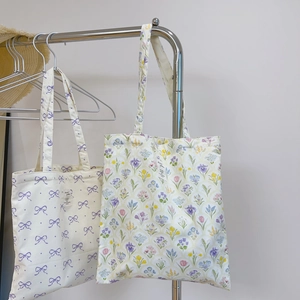 Detail of floral and bow pattern canvas tote bags hanging on a minimalist hanger