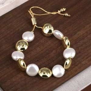 Dettaglio del bracciale con perle piatte bianche, sfere dorate e chiusura regolabile