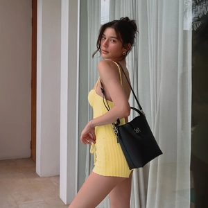 Detailed view of yellow ribbed knit romper paired with a black designer bucket bag