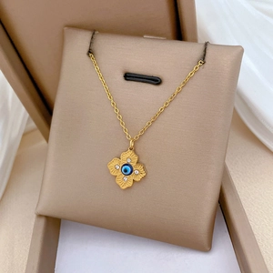 Macro shot of gold clover necklace with evil eye charm and rhinestones on beige cushion