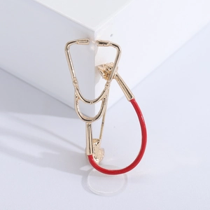 Detailed view of a gold and red stethoscope brooch on a white geometric display stand