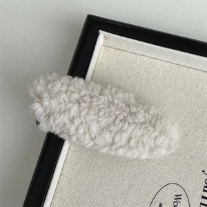Close-up of beige plush teddy faux fur hair clip against a minimalist art background