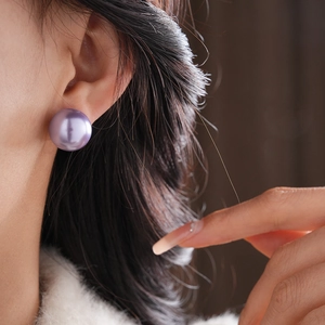 Close-up of a model wearing a large purple pearl earring with a gold-plated finish