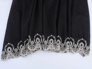 Detail shot of black dress hem featuring intricate white hollow-out floral embroidery