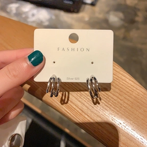 Primer plano de aretes de aro triples entrelazados de plata en tarjeta de moda