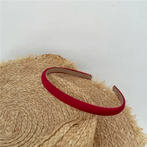 Detail of red fabric headband placed on a straw hat against a white wall background