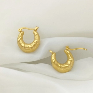 Macro shot of gold U-shaped earrings with fine spiral texture on white silk background